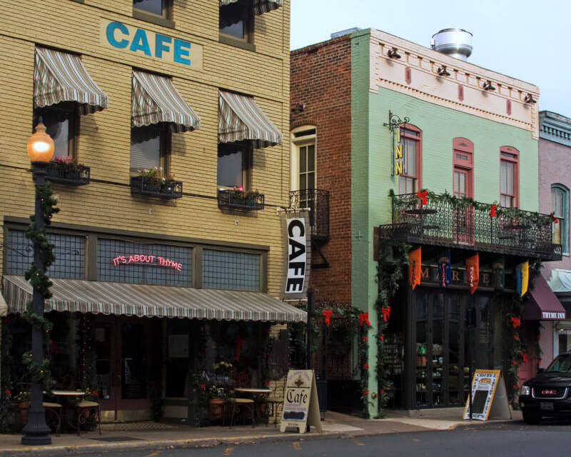 A charming street view with a brick building featuring a café. The café has striped awnings, a neon sign reading