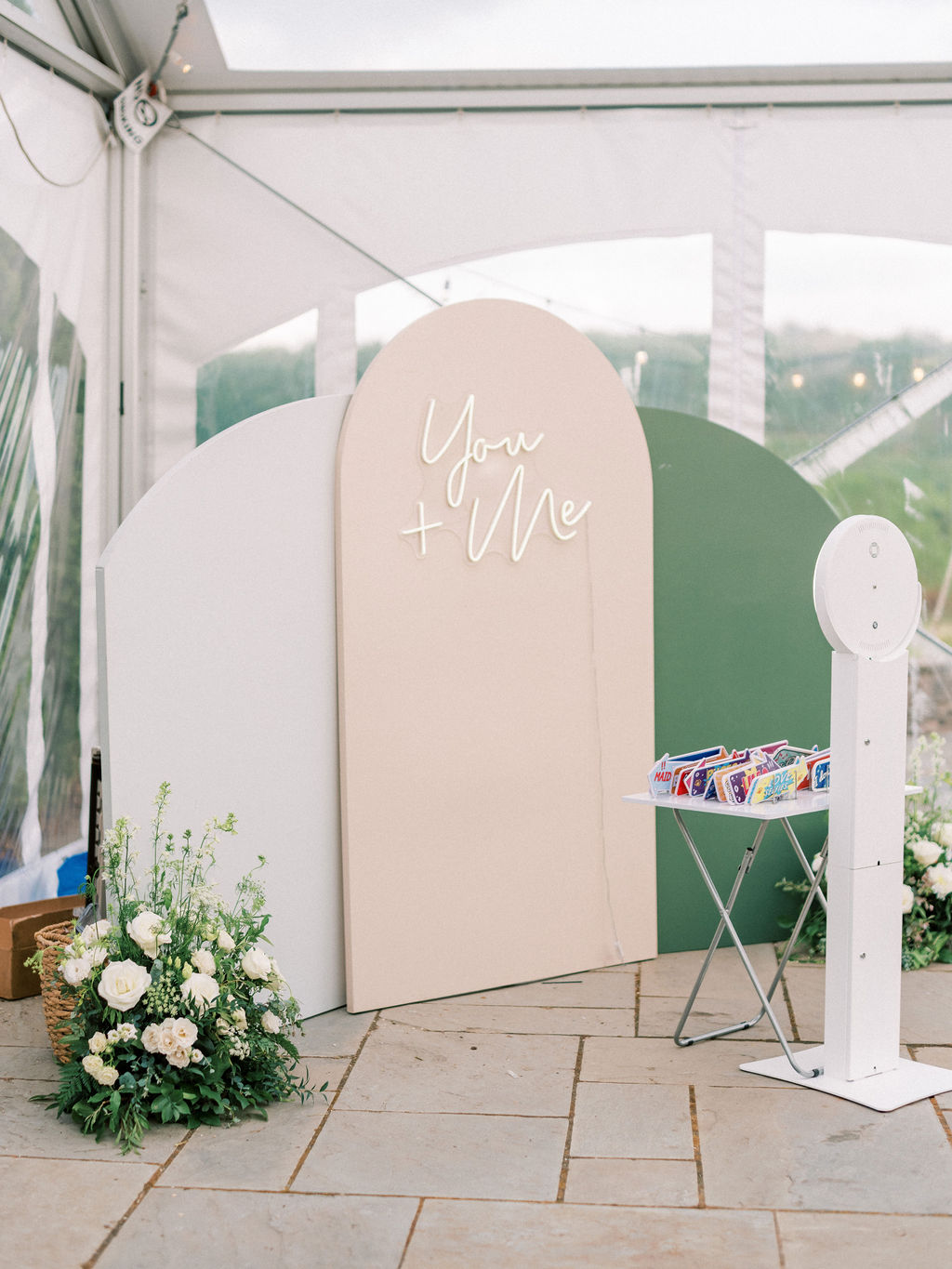 A wedding decoration setup featuring a pastel-colored curved backdrop with a neon sign reading 