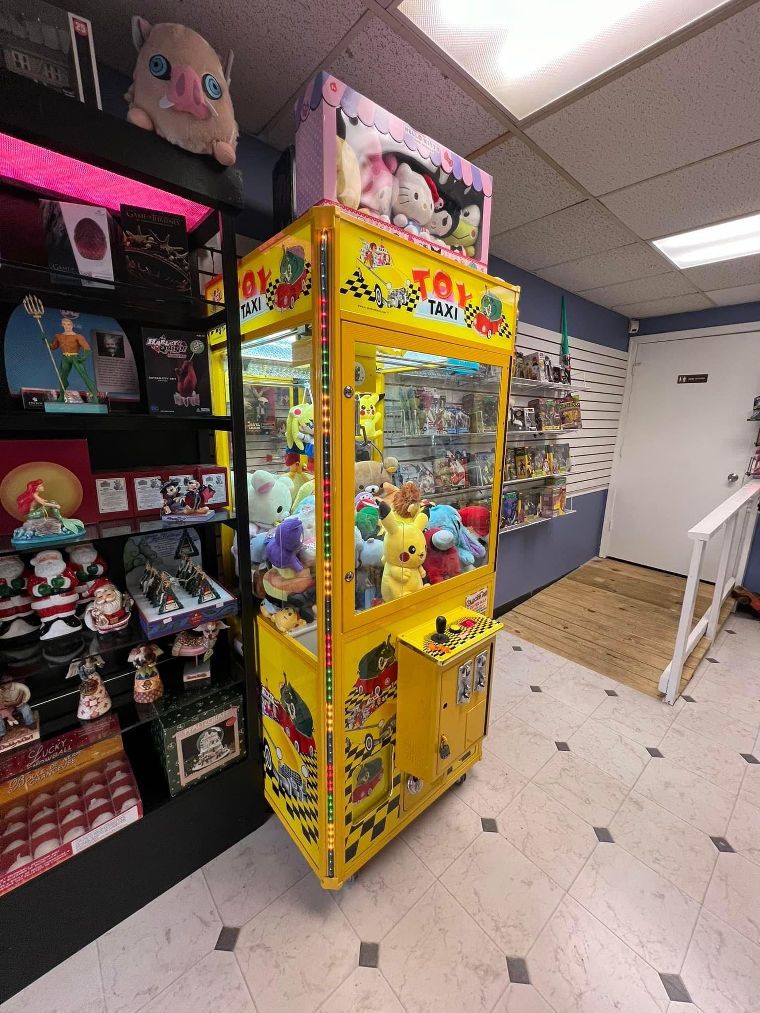 A brightly lit arcade room with a yellow claw machine labeled 
