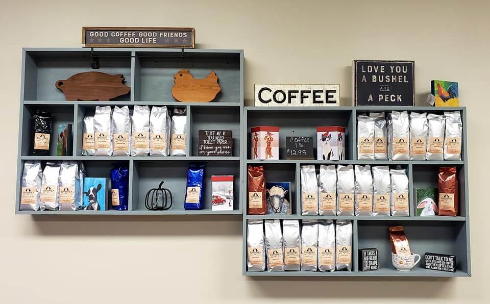 A wall-mounted display of coffee products and decor, including two shelves filled with silver bags of coffee. Signs on the shelves read 