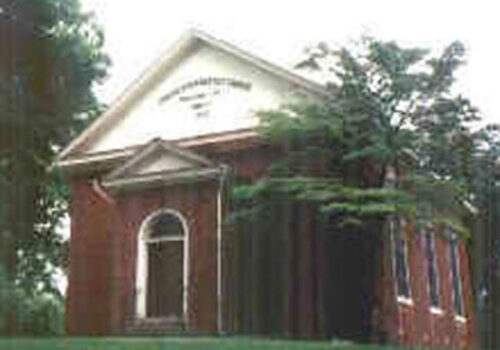 A brick church with a white arched entrance and white triangular upper facade inscribed with the words 