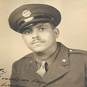 Black and white photo of a man in a military uniform wearing a peaked cap. He has a mustache and is looking directly at the camera. There is handwritten text at the bottom of the photo.