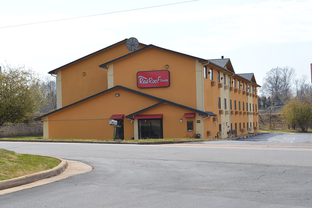 A three-story hotel building painted in yellow with a red awning over the entrance. A sign reads