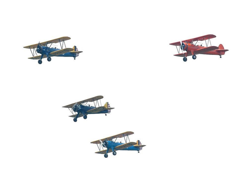 Three vintage biplanes fly in formation against a plain white sky. Two of the planes are blue and yellow, and the third plane is red. Each biplane has an open cockpit and a distinctively classic design with double wings.