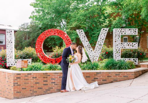 A bride and groom kiss in front of a large, decorative 