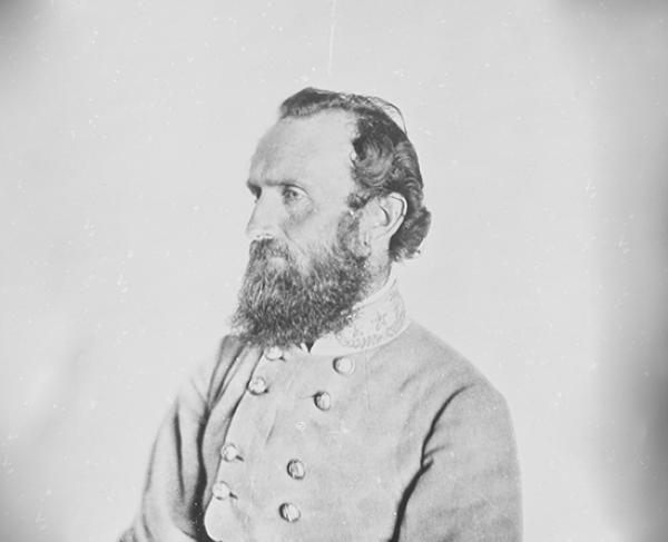 A black and white portrait of a bearded man in a military uniform with double-breasted buttons. He is facing to the right, looking away from the camera. The background is plain and light-colored.