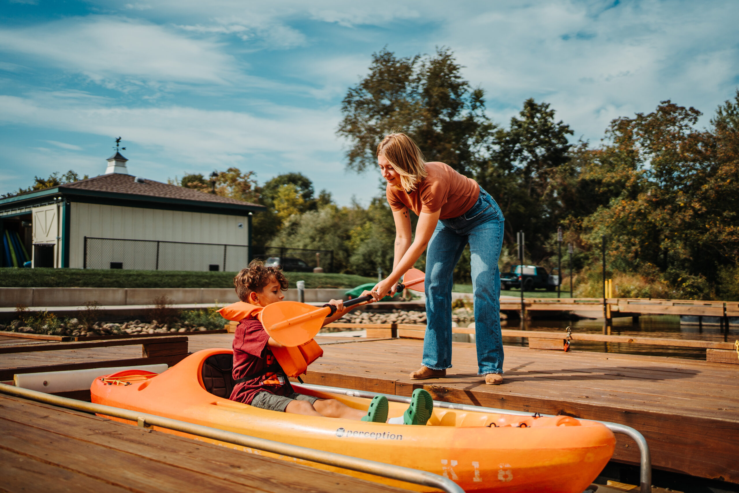 woman handing a young boy a paddle as he sits in a kayak
