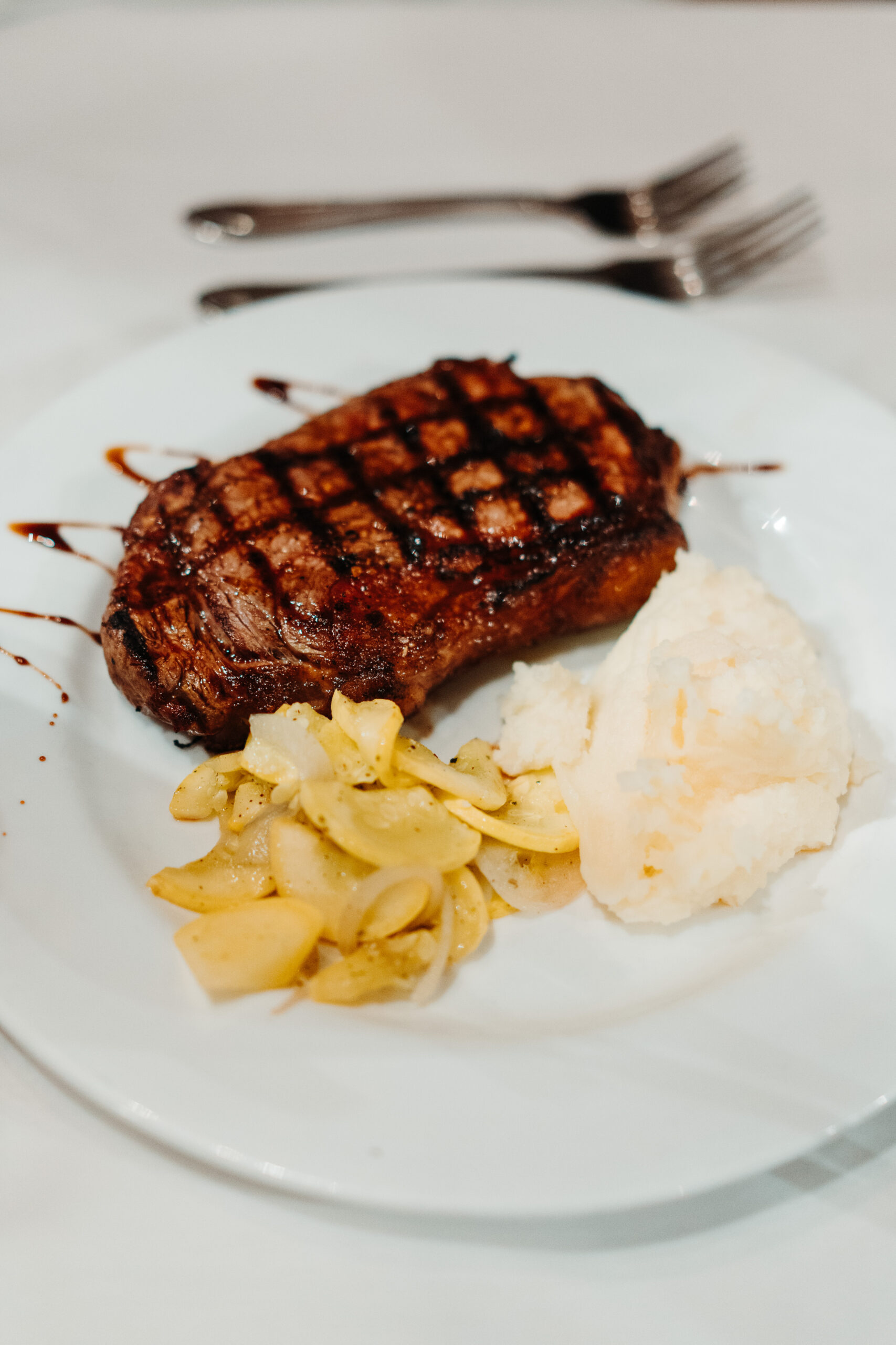steak on a plate garnished with balsamic glaze and side of mashed potatoes and zucchini