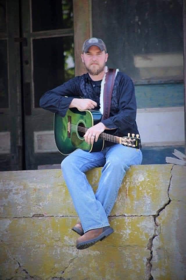 image of Austin Boggs holding a guitar and sitting on a wall