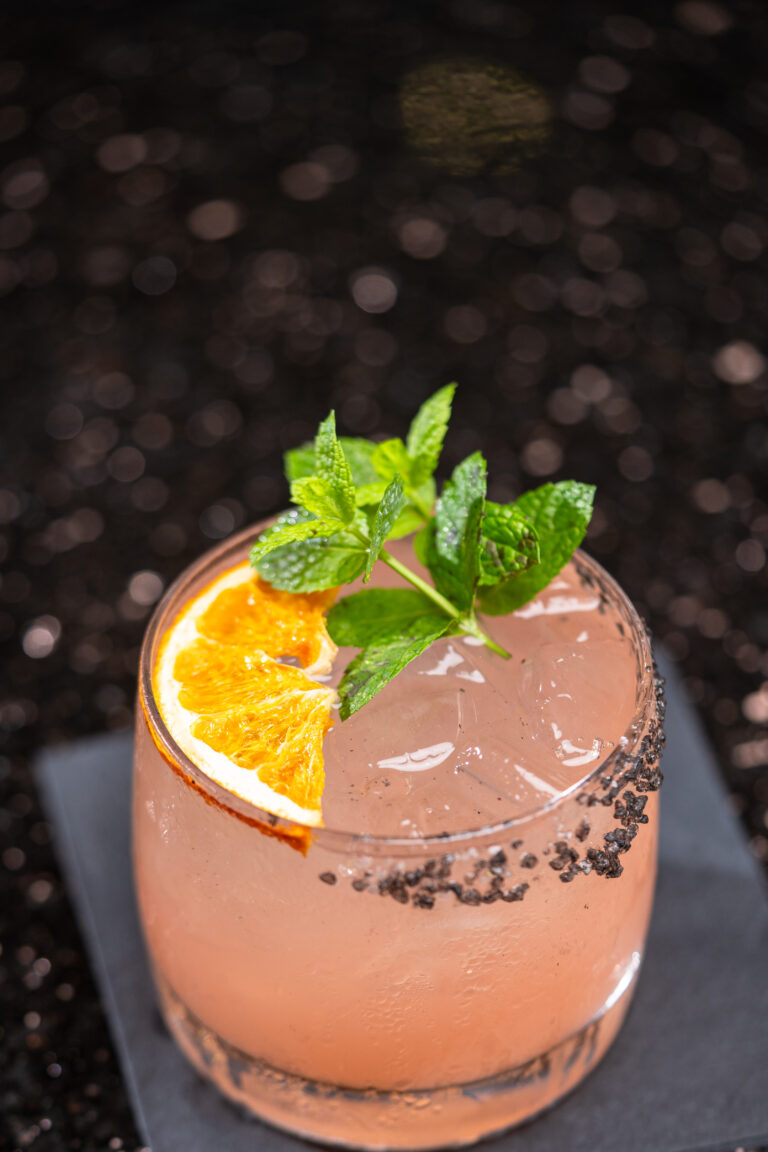 pink mixed drink with a orange slice and green garnish